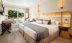 Hotellihuone, jossa on suuri parivuode, istuinryhmä ja parveke näkymällä vihreisiin palmuihin. (Tekoälyn luoma teksti)