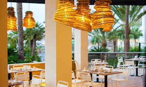 Ulkolkalusteet ravintolassa, riippuvat puuvarjostimet ja taustalla palmuja. (Tekoälyn luoma teksti)