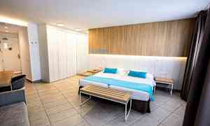 Moderni hotellihuone, jossa on parisänky, puupenkki jalkopäässä ja työpöytä nurkassa. (Tekoälyn luoma teksti)