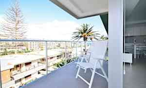 Parveke, jossa valkoiset tuolit ja näkymä rakennuksiin ja palmuihin. (Tekoälyn luoma teksti)