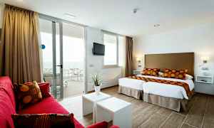 Moderni hotellihuone, jossa kaksi yhden hengen vuodetta, punaiset sohvakalusteet ja parveke merinäköalalla. (Tekoälyn luoma teksti)