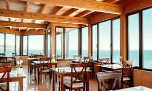 Kahvila, jossa on puisia pöytiä ja tuoleja, suurten ikkunoiden takana näkyy merinäkymä. (Tekoälyn luoma teksti)