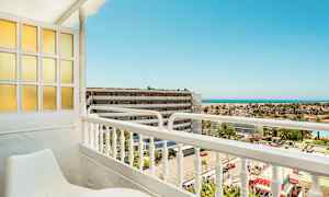 Näkymä parvekkeelta, jossa istuimet, kohti rakennusta ja merta taustalla. (Tekoälyn luoma teksti)