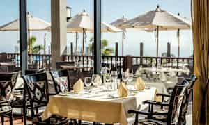 Kattojen ravintolassa katetulla pöydällä näkyy terassi aurinkovarjoilla ja merellä. (Tekoälyn luoma teksti)