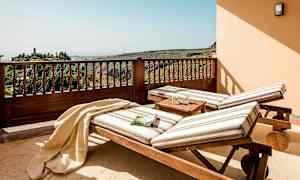 Kaksi raidallisilla tyynyillä varustettua aurinkotuolia seisoo terassilla, josta avautuu näkymä vehreille kukkuloille. (Tekoälyn luoma teksti)