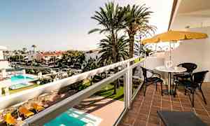 Näkymä parvekkeelta, jossa on istuimet ja aurinkovarjo, taustalla uima-allas ja palmuja. (Tekoälyn luoma teksti)