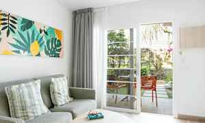 Olohuoneen ympäristö, jossa harmaa sohva, koristetyynyt, värikäs seinätaide ja lasiovi, joka johtaa terassille. (Tekoälyn luoma teksti)