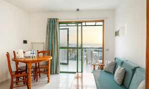 Huone, jossa ruokapöytä ja tuolit, sohva ja lasiovi parvekkeelle. (Tekoälyn luoma teksti)