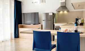 Keittiö, jossa tiskipöytä, kaksi sinistä tuolia, jääkaappi ja televisio puukaapin luona. (Tekoälyn luoma teksti)