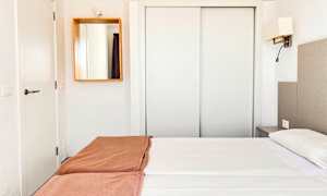 Hotellihuone, jossa valkoiset sisusteet, parivuode valkoisilla lakanoilla ja ruskeilla peitteillä sekä peili seinällä. (Tekoälyn luoma teksti)