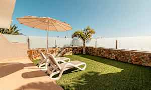 Terassi, jossa on kaksi aurinkotuolia, aurinkovarjo ja tekonurmikko. (Tekoälyn luoma teksti)