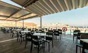 Ulkoterassilla pöytiä ja tuoleja, näkymä kaupunkiin ja merelle. (Tekoälyn luoma teksti)