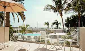 Parveke, jossa aurinkotuoleja ja pöytä tuoleineen, näkymä uima-altaalle ja palmuihin. (Tekoälyn luoma teksti)