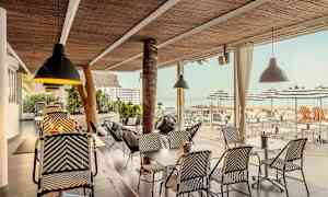 Ulkoterassi rottinkikalusteilla ja kattovalaisimilla, näkymä merelle ja päivänvarjoille. (Tekoälyn luoma teksti)