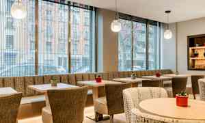 Moderni ja valoisasti sisustettu kahvila, jossa on suuret lasi-ikkunat, pöytiä ja tuoleja sekä pieniä kasveja koristeena. (Tekoälyn luoma teksti)