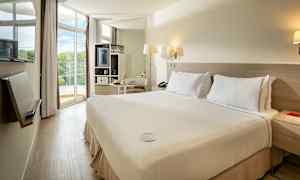 Hotellihuone, jossa on parisänky ja vaalea sisustus, suuret ikkunat ja parveke, jolta on näkymät. (Tekoälyn luoma teksti)