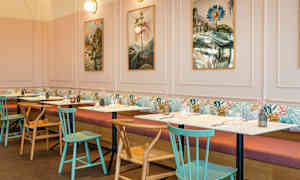 Ravintola, jossa pöydät ja tuolit, kuvia seinällä ja pehmeitä sohvia seinän vieressä. (Tekoälyn luoma teksti)