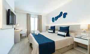 Hotellihuone, jossa kaksi sänkyä ja merellinen teema, siniset vuodevaatteet ja koristeelliset tyynyt. (Tekoälyn luoma teksti)