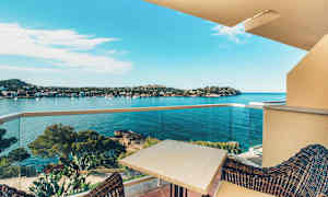 Näkymä parvekkeelta lahteen, jossa on kirkasta sinistä vettä ja ympäröivää mäkistä maastoa ja puita. Parvekkeella on pöytä ja tuolit etualalla. (Tekoälyn luoma teksti)