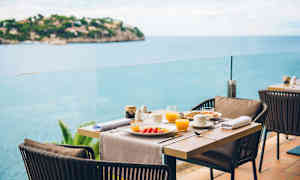 Katettu ruokapöytä, jossa lautasia ja laseja terassilla merinäköalalla. (Tekoälyn luoma teksti)