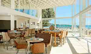 Nykyaikaisesti sisustettu ravintolatila, jossa suuret lasi-ikkunat tarjoavat näkymän rannalle ja merelle. (Tekoälyn luoma teksti)