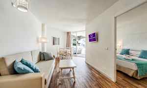 Hotellihuoneen kuva, jossa on olohuone, sohva, ruokapöytä ja viereinen makuuhuone. (Tekoälyn luoma teksti)