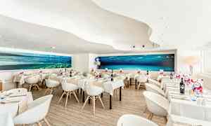 Moderni ravintola, jossa on valkoiset tuolit ja pöydät sekä suuri vedenalainen maalaus seinällä. (Tekoälyn luoma teksti)