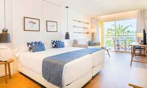 Moderni hotellihuone, jossa kaksi vuodetta ja sinisiä yksityiskohtia sekä parveke näkymällä palmuihin. (Tekoälyn luoma teksti)