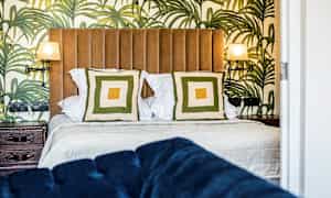 Makuuhuone, jossa on sänky, kaksi tyynyä ja suuria vihreitä lehtiaiheita sisältävä tapetti. (Tekoälyn luoma teksti)