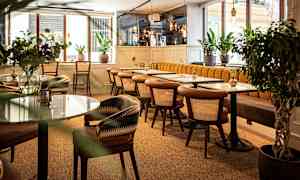 Moderni kahvila, jossa on puutuoleja ja marmoripöytiä, ympäröitynä vihreillä kasveilla. (Tekoälyn luoma teksti)