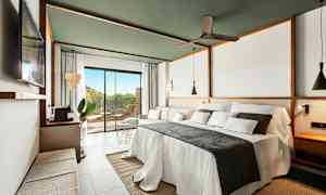 Moderni hotellihuone, jossa on suuri pedattu sänky, sohva ja suuri ikkuna terassille. (Tekoälyn luoma teksti)