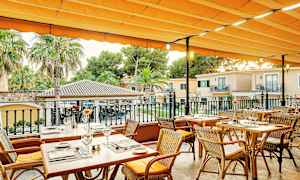 Ulkoterassi, jossa on katetut puupöydät ja tuolit oranssin markiisin alla. (Tekoälyn luoma teksti)