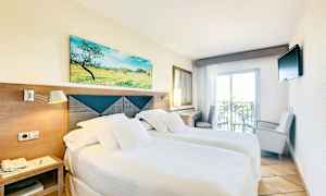 Hotellihuone, jossa on kaksi yhden hengen vuodetta, vaaleat vuodevaatteet, päätylaudan yläpuolella oleva taulu, pieni parveke ja seinälle kiinnitetty televisio. (Tekoälyn luoma teksti)