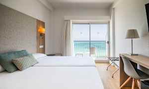 Hotellihuone, jossa kaksi vuodetta, kirjoituspöytä ja näkymä merelle lasioven kautta. (Tekoälyn luoma teksti)