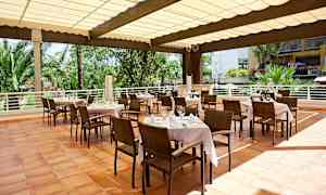 Ulkoterassi katettujen pöytien, tuolien ja puutarhaympäristön kanssa taustalla. (Tekoälyn luoma teksti)