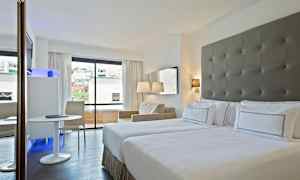 Hotellihuone kahdella sängyllä, ikkunalla, josta on näkymä kaupunkiin, sekä istuinalueella, jossa pöytä ja tuoli. (Tekoälyn luoma teksti)