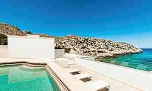 Ulkouima-allas rakennuksen yhteydessä, näkymä merelle ja kiviseen vuoristoon kirkkaan sinisen taivaan alla. (Tekoälyn luoma teksti)