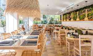 Ravintola, jossa on puiset pöydät, rottinkituolit ja koristeelliset valaisimet. (Tekoälyn luoma teksti)