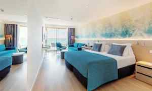 Hotellihuone, jossa on parivuode, sininen sisustus ja oleskeluryhmä. Iso ikkuna tarjoaa näkymän merelle. (Tekoälyn luoma teksti)