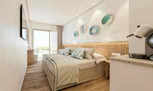 Moderni hotellihuone, jossa on parivuode, koristeelliset koristekulhot seinällä, kahvikone ja suuret lasiovet, jotka johtavat parvekkeelle. (Tekoälyn luoma teksti)