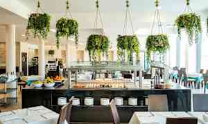 Ravintola, jossa pöytiä, tuoleja ja buffet sekä riippuvia vihreitä kasveja. (Tekoälyn luoma teksti)