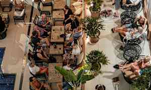 Ryhmä ihmisiä istuu pöytien ja sohvien ääressä ulkona olevassa loungessa. (Tekoälyn luoma teksti)