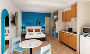 Hotellihuone, jossa parivuode, sininen seinä, ruokapöytä ja keittiö. (Tekoälyn luoma teksti)