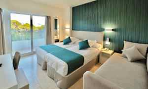 Hotellihuone, jossa on parivuode, sohva, kirjoituspöytä ja ikkuna, josta näkymä vehreään maisemaan. (Tekoälyn luoma teksti)