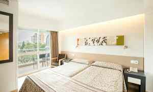 Hotellihuone, jossa on kaksi yhden hengen vuodetta, koristeltu kuvioiduilla päiväpeitteillä. On kalustettu parveke, joka avautuu ulkoalueelle. (Tekoälyn luoma teksti)