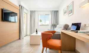 Valoisa, moderni hotellihuone, jossa on sohva, tuoli, televisio, kirjoituspöytä ja suuret ikkunat. (Tekoälyn luoma teksti)