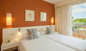 Kuva hotellihuoneesta, jossa on kaksi erillistä vuodetta, koristetyynyjä, taidetta seinällä ja parveke näkymällä. (Tekoälyn luoma teksti)