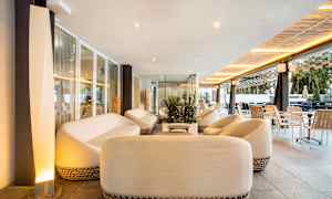 Rentoutumisalue, jossa on valkoisia sohvia ja pöytiä, lasiseinien ympäröimänä modernilla sisustuksella. (Tekoälyn luoma teksti)