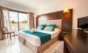 Hotellihuone, jossa on kaksi erillistä vuodetta, televisio ja parveke taustalla. (Tekoälyn luoma teksti)