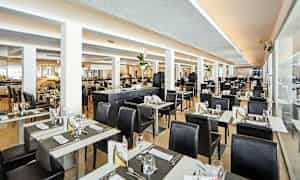 Valoisa ja moderni ravintola-alue, jossa on katettuja pöytiä ja mustia tuoleja. (Tekoälyn luoma teksti)